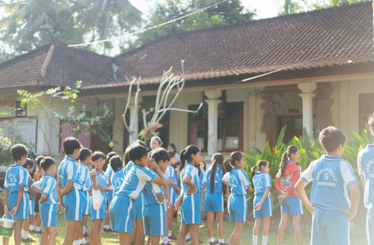 Children gathered in sports uniforms for outdoor school activities by a traditional building.